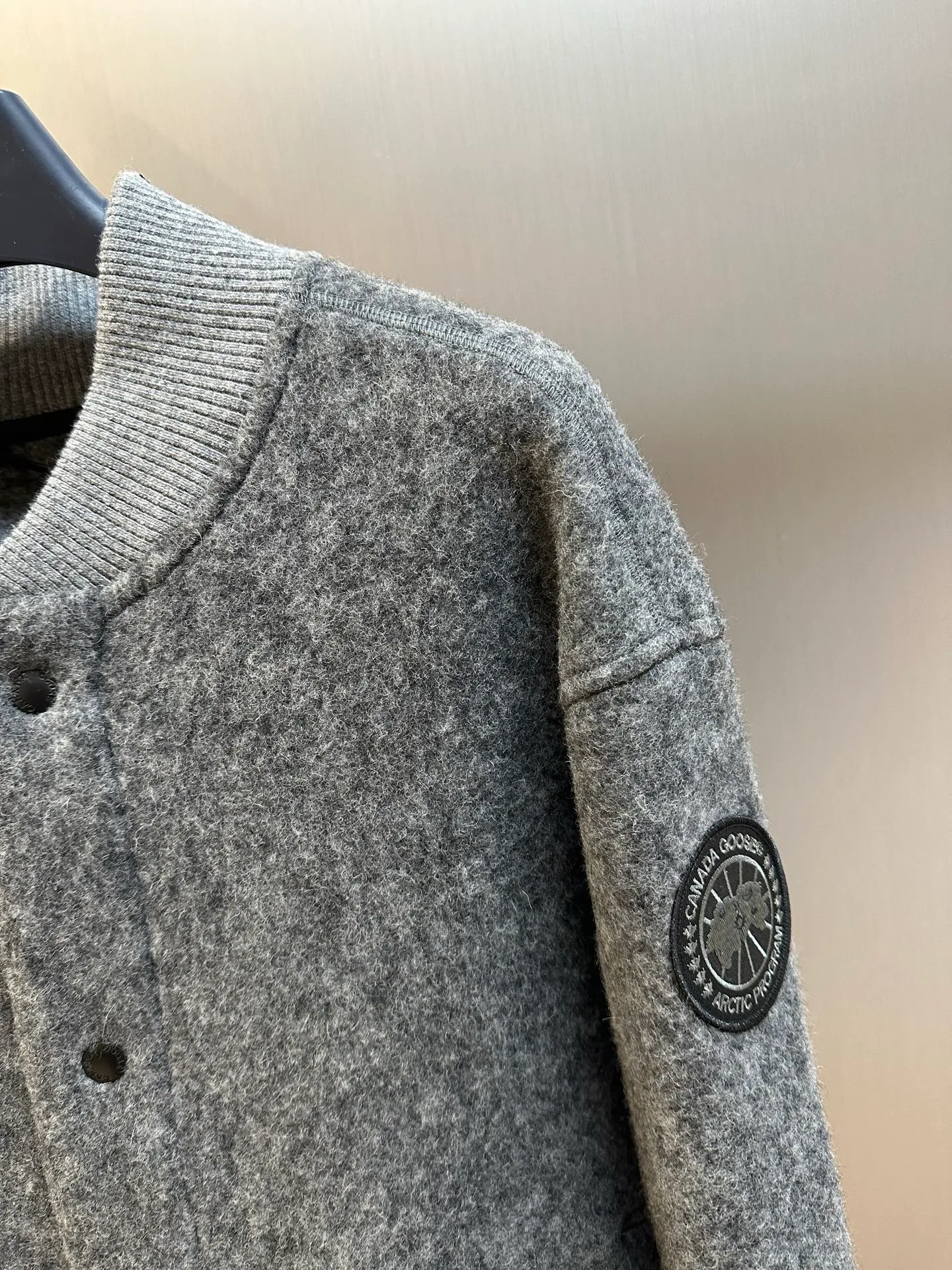 P770 Canada Goose Fleece Badge Button Jacket The main fabric of this jacket is light gray wool blend fabric to improve the fabric's wear resistance, wrinkle resistance and warmth. Wool provides good warmth and a natural feel, while blended fibers enhance the fabric's practicality and durability.  The cutting process needs to ensure that the texture and color of the fabric are evenly distributed, especially with this light gray tone, to avoid chromatic aberrations. The stretchability of wool-blend fabrics needs to be taken into consideration when cutting pieces to ensure dimensional stability of the finished garment.  Use a sewing needle and thread suitable for wool-blend fabrics to avoid damage to the fabric during sewing. The sewing stitches are even and firm to prevent thread stripping.  The temperature needs to be controlled during ironing to avoid high temperature damage to the fabric while keeping the fabric smooth and crisp. The front and back body parts, sleeves and other main parts are stitched with flat seams to ensure a smooth silhouette. Align the fabric texture at the splices to keep the look neat.  The white circular armband on the left arm is an important part of the brand identity and is finely sewn to ensure it is strong and flat.  size：s m l xl